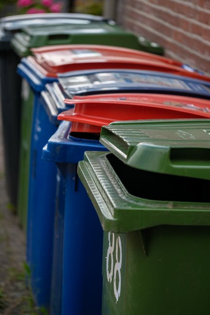 A large pile of black rubbish bags filled with waste, placed on a pavement adjacent to a modern building with reflective tiled surfaces. Some of the bags are partially opened, revealing plastic bottle